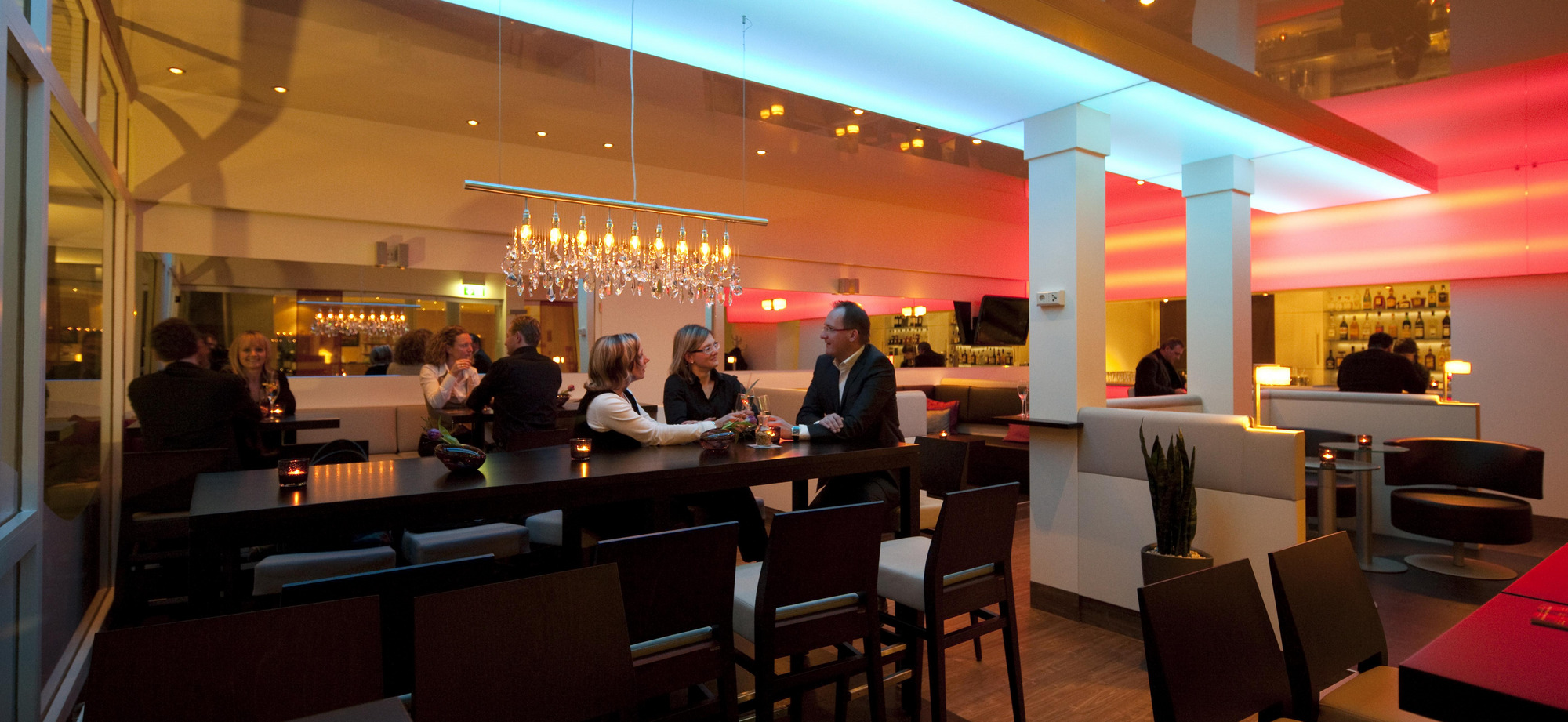 Restaurant- und Barbereich mit Theke, warmem Licht, Flaschenregalen und Gästen im Gespräch.