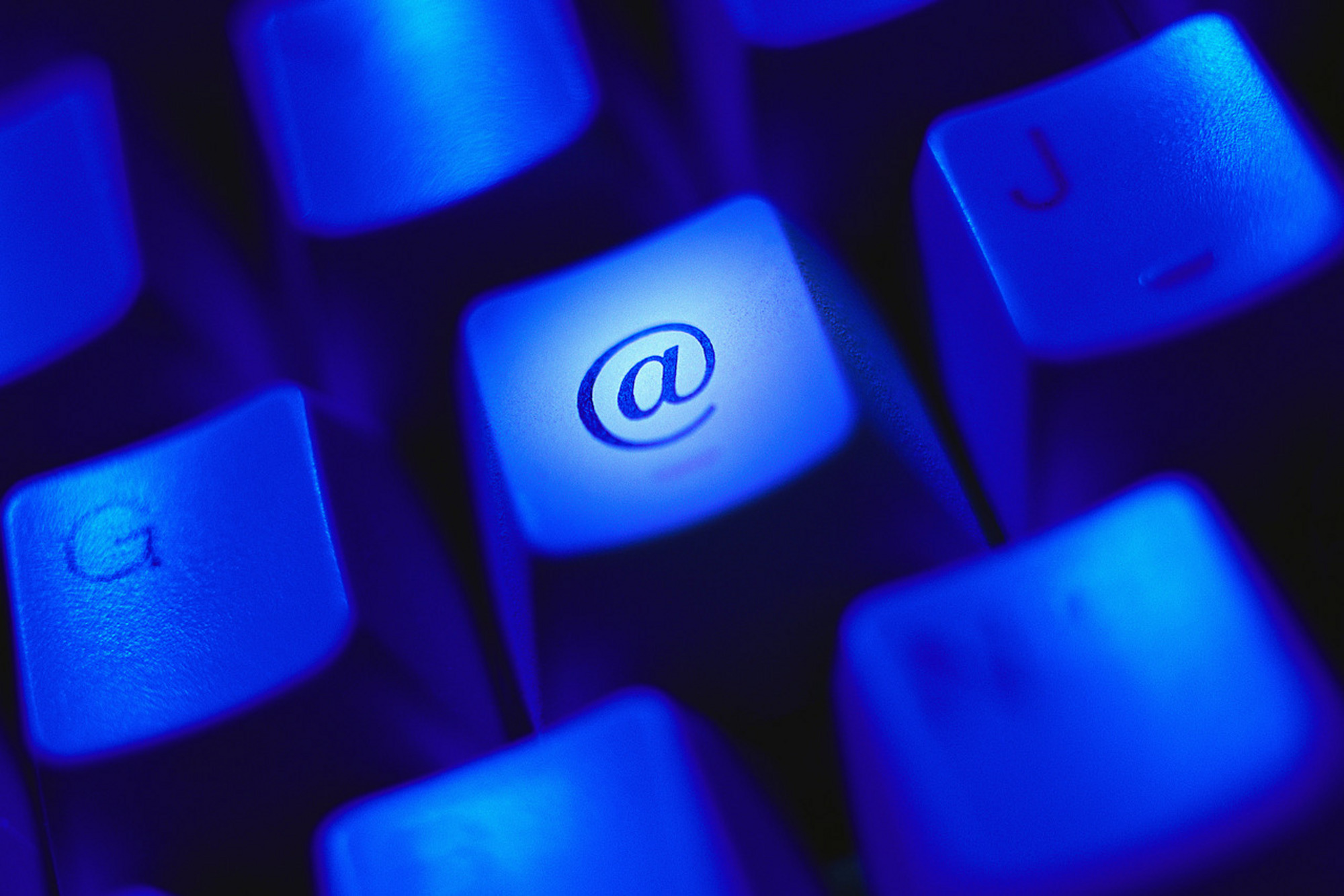 Tastatur mit blauer Hintergrundbeleuchtung, Fokus auf hell erleuchtete „@“-Taste.