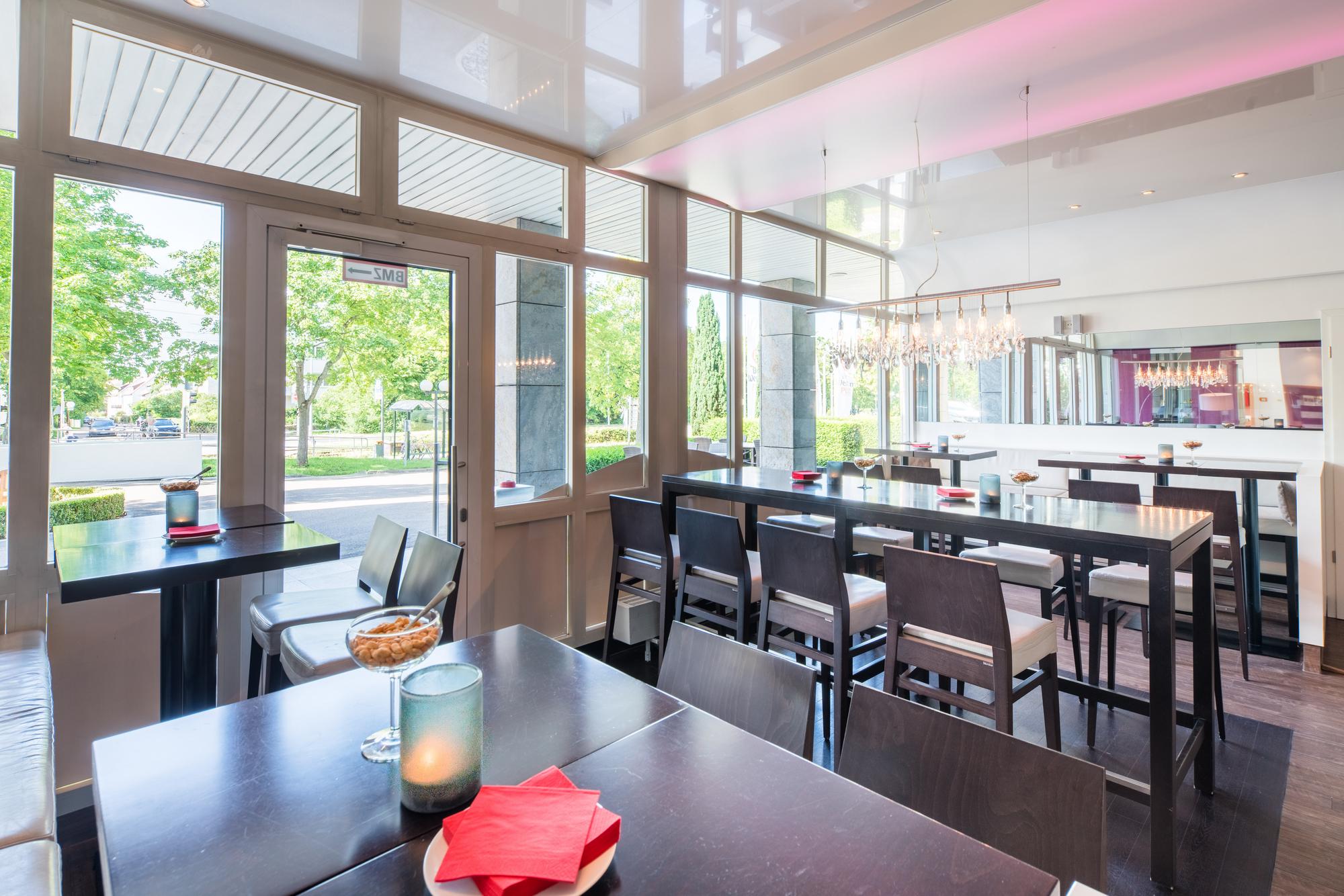 Helle Bar mit großen Fenstern, mehreren Tischen und ordentlich angeordneten Stühlen.