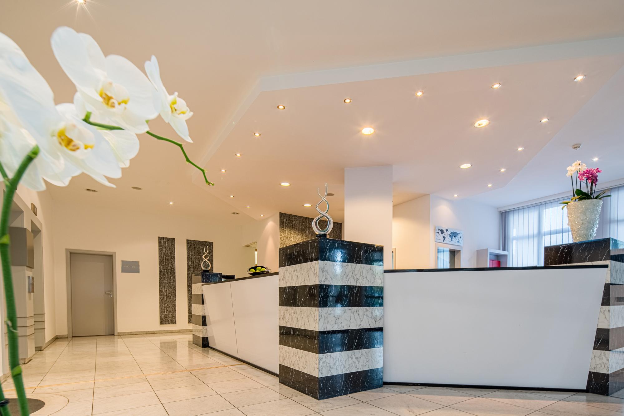 Moderne Rezeption mit weißem Tresen, schwarzen Streifen, Hängelampen, Pflanzen und natürlichem Lichteinfall.