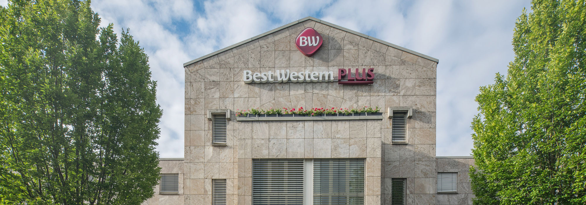 Außenansicht eines Hotelgebäudes mit Best Western Plus Logo und umgeben von Bäumen.