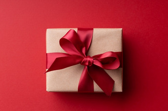 Geschenkbox in braunem Papier mit roter Schleife auf rotem Hintergrund.